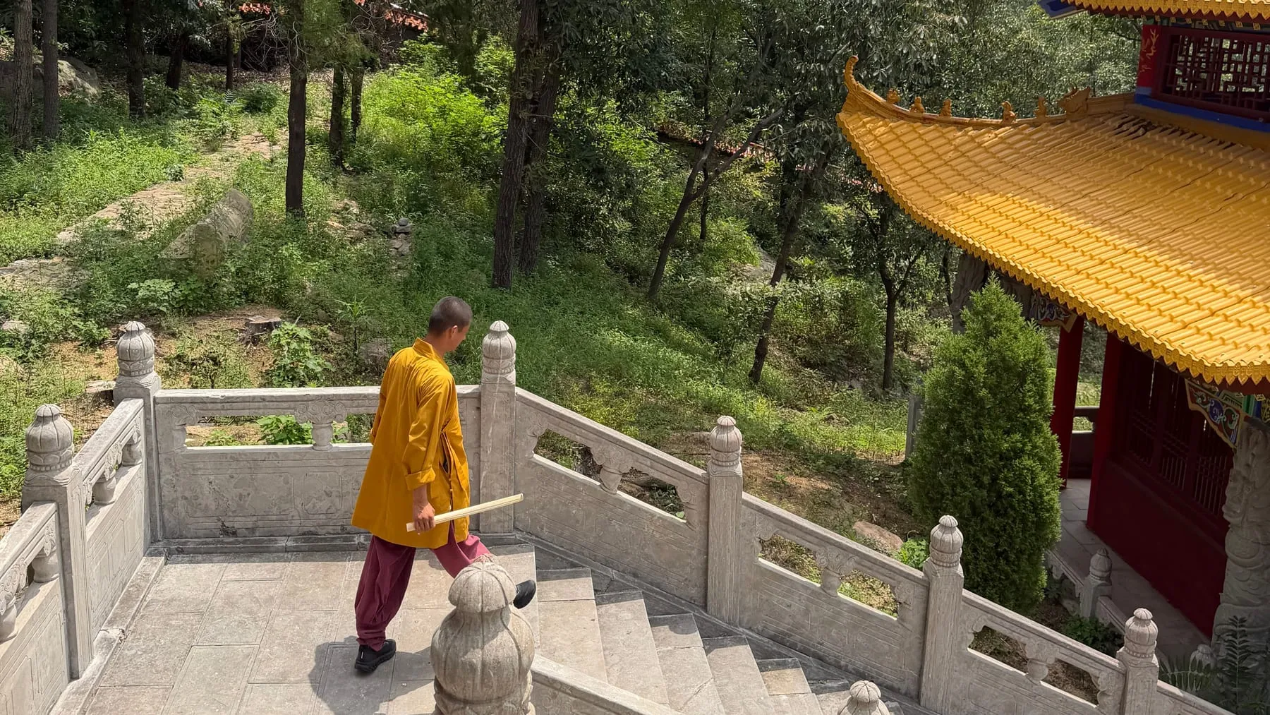 Le maître, en robe safran, descend les escaliers de marbre d’un temple aux toits dorés, dans les montagnes près de Tengzhou.