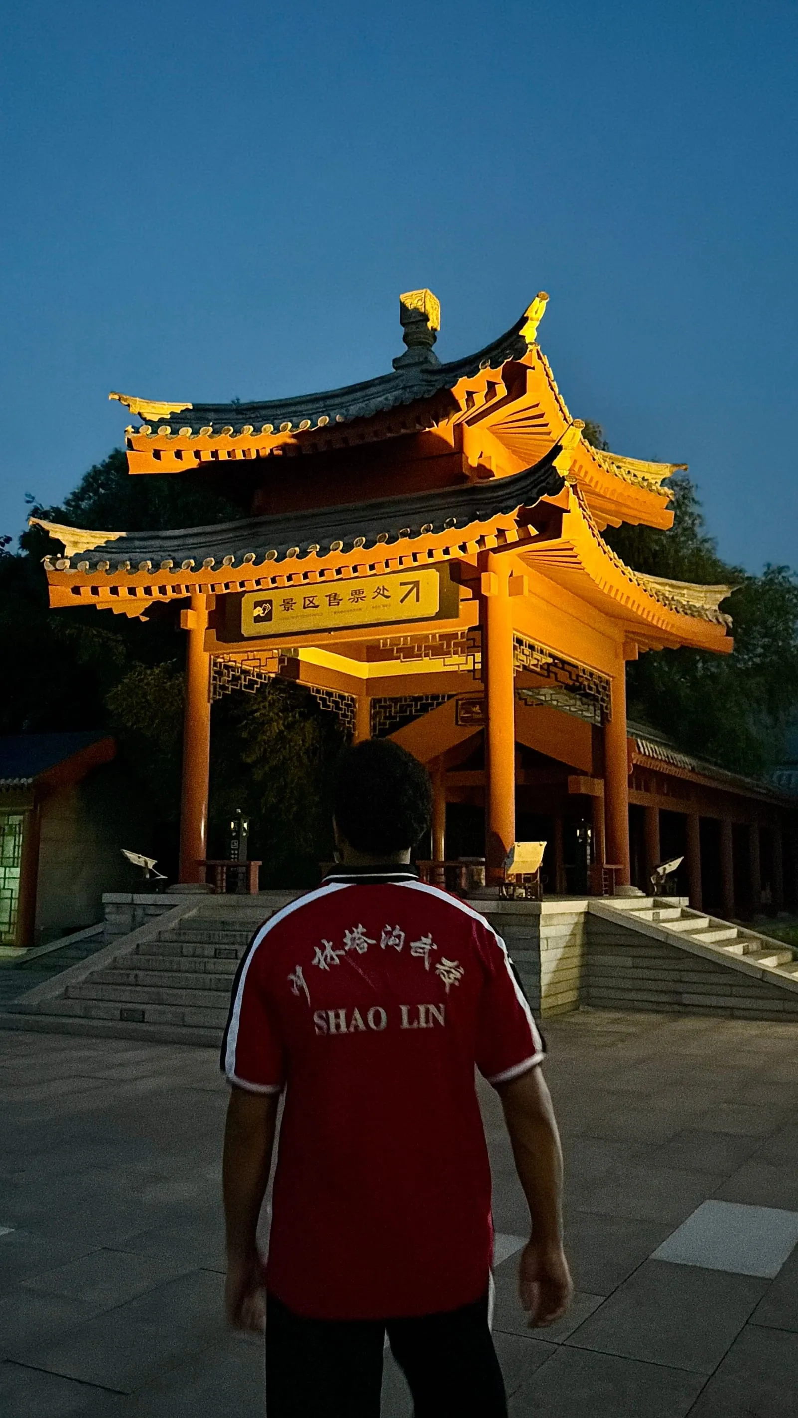 Un portique chinois aux toits dorés, éclairé au crépuscule sous un ciel bleu profond.
