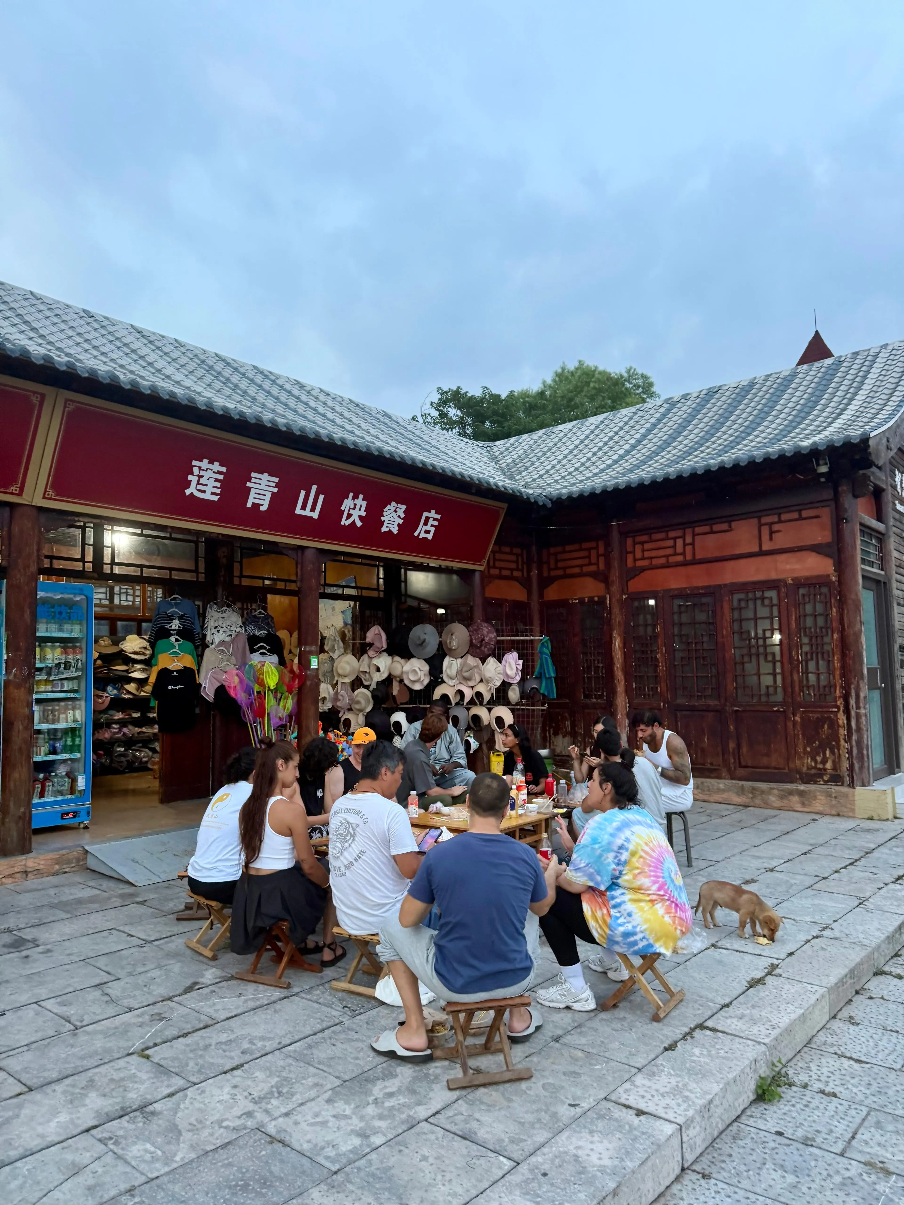 Des voyageurs partagent un repas autour de petites tables en plein air, devant un bâtiment traditionnel chinois.